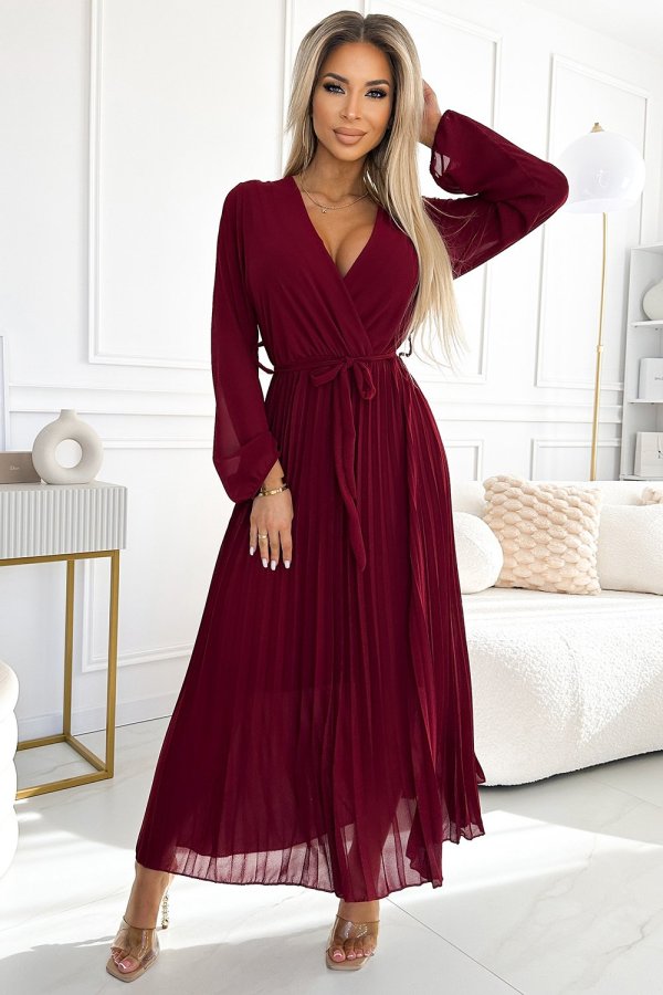 Modelka prezentuje elegancką sukienkę maxi w głębokim odcieniu bordo, która idealnie podkreśla sylwetkę. Kobieta na zdjęciu nosi sukienkę maxi z delikatnym wiązaniem w talii, dodającym jej szyku i klasy.